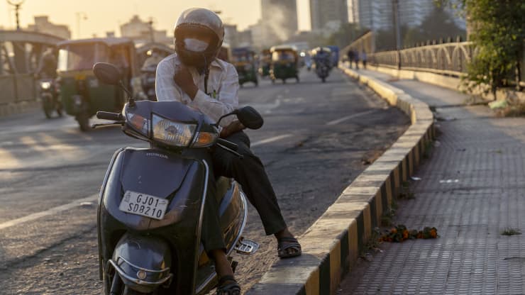 Một người đi xe máy đeo mặt nạ bảo vệ khi ngồi bên lề đường tại Sabarmati Riverfront ở Ahmedabad, Ấn Độ - Ảnh: Bloomberg